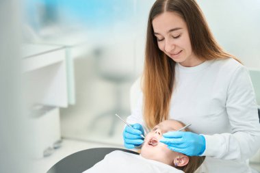 Azot eldivenli konsantre pedodontist diş ve ağız aynası olan küçük kızın dişlerini inceliyor.