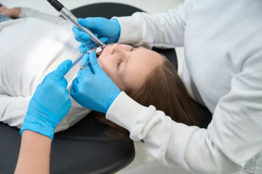 Tek kullanımlık nitril eldivenli pedodontist. Hemşire eşliğinde küçük bir kızın diş boşluğunu deliyor.