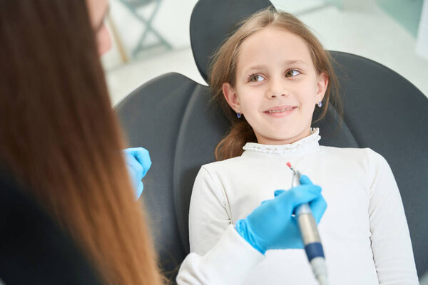 Pediatric doctor in nitrile gloves holding dental handpiece with nylon bristle polishing brush over smiling child