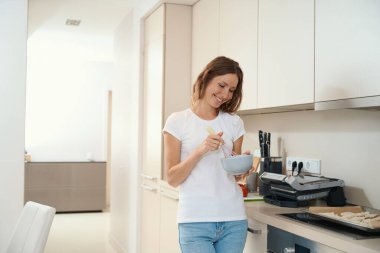 Mutfak yüzeyine yakın duran mutlu ev hanımı tabak ve çırpıcıyla parşömen ve fırında hamur işleriyle uğraşırken