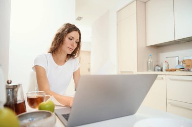 Mutfakta aperatiflerin yanındaki belgelerle uzaktan kumandayla çalışan odaklanmış bir kadın.