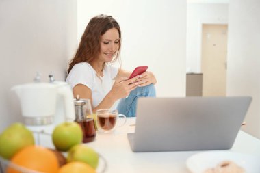 Neşeli bayan başka bir aletin önünde mutfaktayken telefonla içeriği izlemekle meşgul.