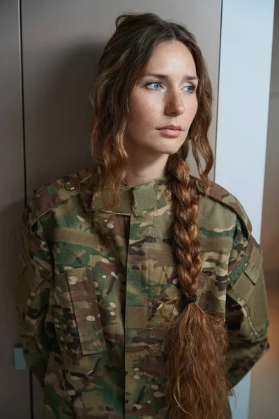 Sad lady with long braided hair is standing by the wardrobe while her gaze is directed to the side
