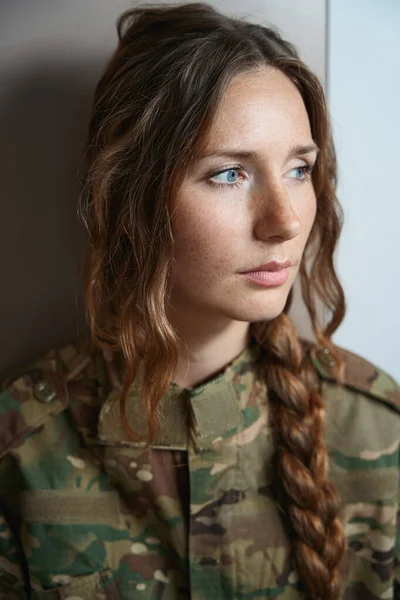 Serious lady with blue eyes stands against the wall while her gaze is directed to the side