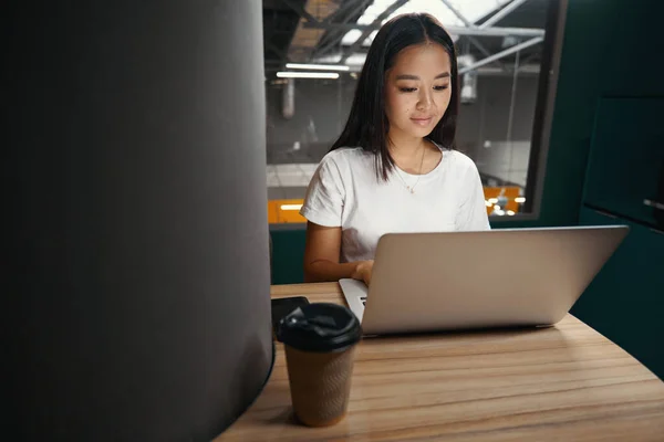 Waist up portrait of happy cheerful Asian office worker is sitting at the desk and reading something on computer in open space office