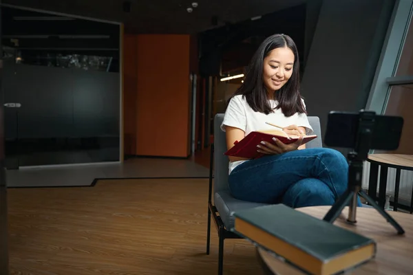 Waist up portrait of happy smiling woman is learning online while using mobile phone in the modern office