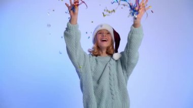 Noel zamanı. Noel Baba şapkasıyla dans eden, menekşe arka planında konfeti olan genç bir kız.