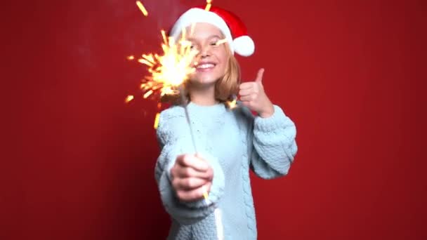Gelukkig klein meisje in Santa Claus cap houden bengal licht op de rode achtergrond — Stockvideo