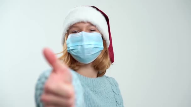 快乐的年轻女孩戴着圣诞老人帽，戴着医疗面具，看起来像 — 图库视频影像