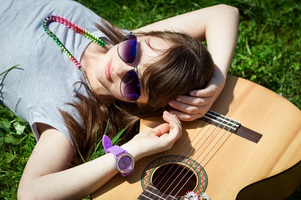 Dívka s kytarou, ležící na trávě — Stock fotografie