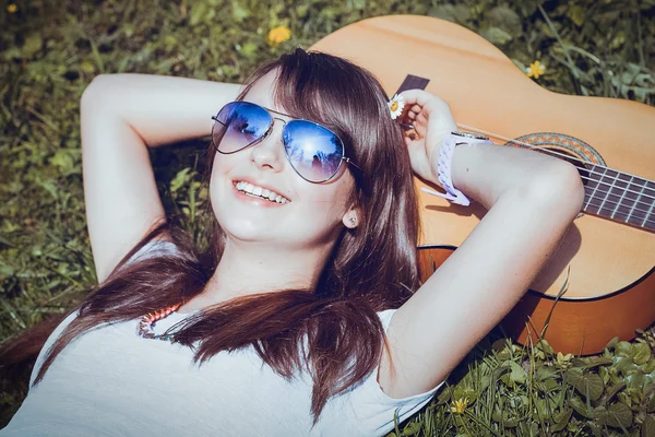 Дівчина з гітарою лежить на траві — стокове фото