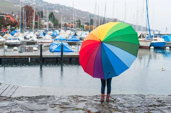 Child under big colorful umbrella watching the rain on the lake, view from the back — Stock Photo, Image