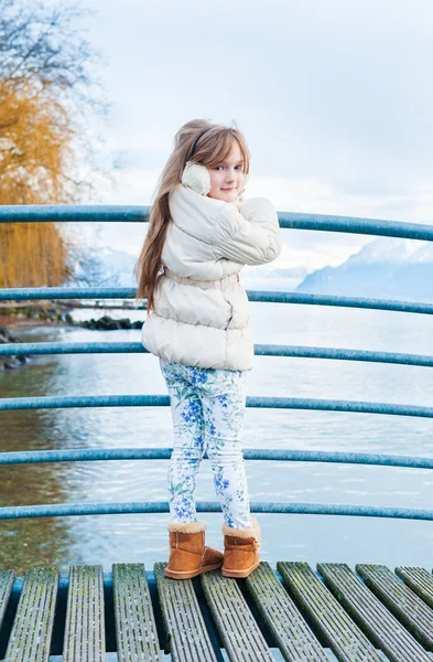 Roztomilá holčička pózuje venku, stojící u jezera s horami — Stock fotografie