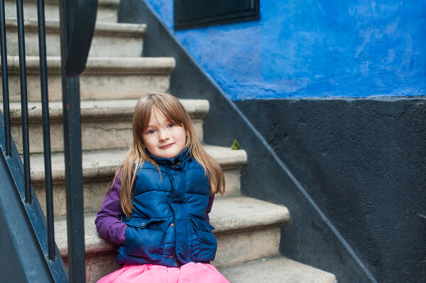 Cute little girl sitting on stairs against blue wall