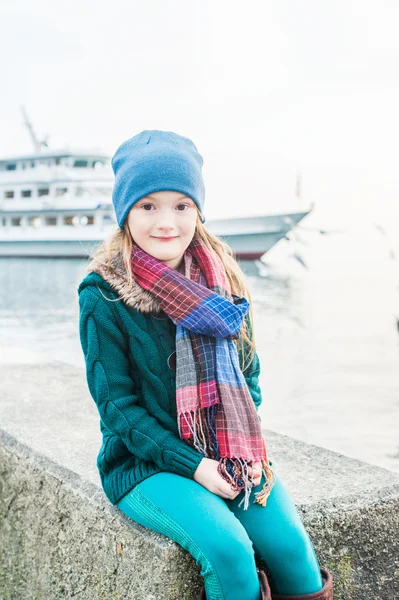 Retrato de uma menina bonita em um tempo frio ao lado do lago, vestindo, casaco verde e calças, chapéu e cachecol — Fotografia de Stock