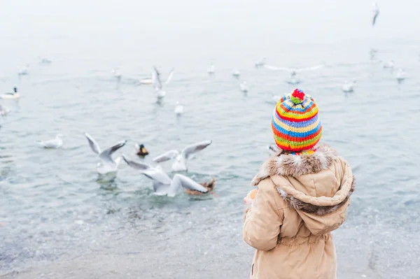 Cute little girl feeding birds on a cold day — Stockfoto