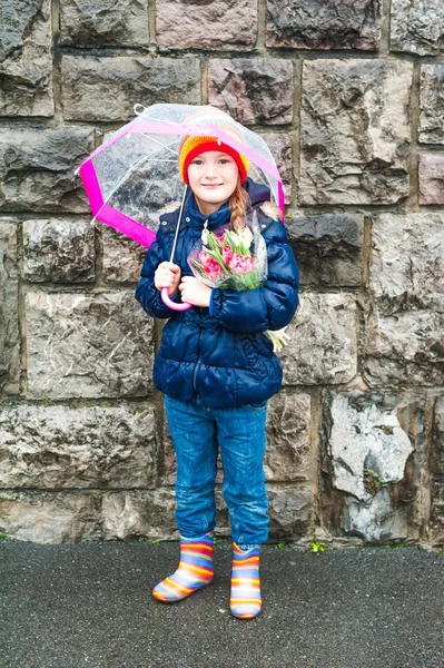 Portrait of a cute little girl on a rainy day, holding, umbrella and bouquet of pink tulips — Stock Photo, Image