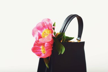 Üzerinde pembe şakayık çiçekleri olan küçük siyah deri çanta.