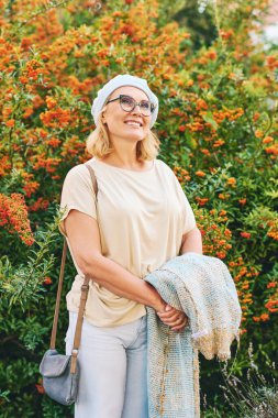 Açık havada mutlu orta yaşlı bir kadının portresi parlak turuncu ateş dikenli meyvelerin yanında poz veriyor (Pyracantha coccinea)