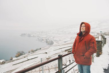 Orta yaşlı bir adamın açık hava portresi. Karlı mahzenlerin kış manzarasının tadını çıkarıyor.