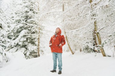 Orta yaşlı bir adamın açık hava portresi. Kış ormanlarında güzel bir gün geçiriyor, kar altında yürüyor, kırmızı turuncu ceket giyiyor.