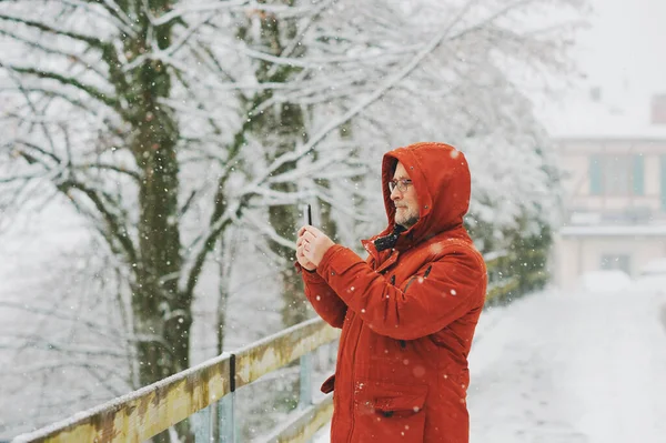 中年男子手持智能手机 为社交媒体拍照或录像 冬季降雪天气 — 图库照片