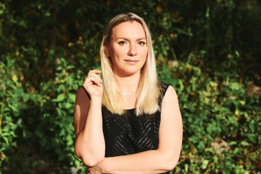 Sarışın, orta yaşlı bir kadının açık havada çekilmiş fotoğrafı. Doğrudan kameraya bakıyor.