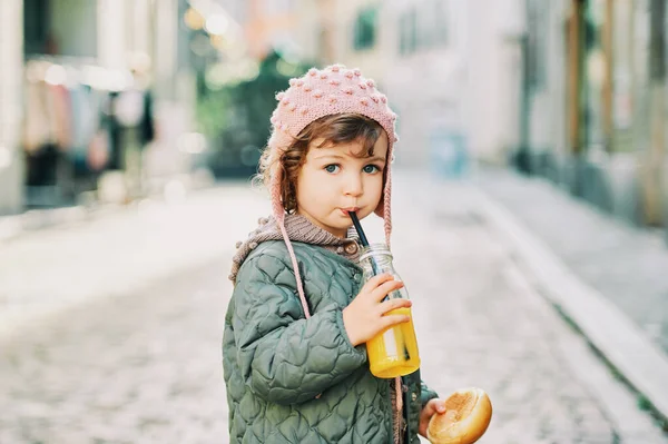 一个可爱的小女孩拿着牛奶面包包 喝着瓶子里的橙汁 在户外的肖像 — 图库照片