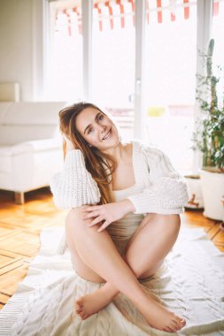 20 yaşında, yerde dinlenen, rahat pijama ve beyaz örülü hırka giyen genç bir kızın kapalı bir portresi.