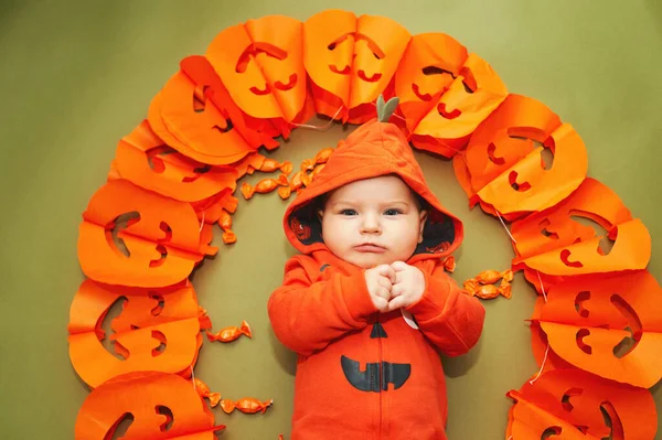 カボチャの庭の隣に緑の背景に横たわっている愛らしい赤ちゃんのハロウィーンの肖像画 — ストック写真