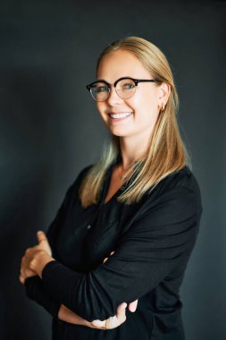 Sarı saçlı, gözlüklü, koyu arkaplanda poz veren güzel bir genç kadın portresi.