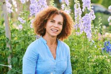 50 yaşında güzel bir kadının açık hava portresi. Çiçek parkında ya da bahçede güzel bir günün tadını çıkarıyor. Mutlu ve sağlıklı bir yaşam tarzı.