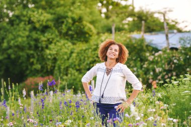 50 yaşında güzel bir kadının açık hava portresi. Çiçek parkında ya da bahçede güzel bir günün tadını çıkarıyor. Mutlu ve sağlıklı bir yaşam tarzı.