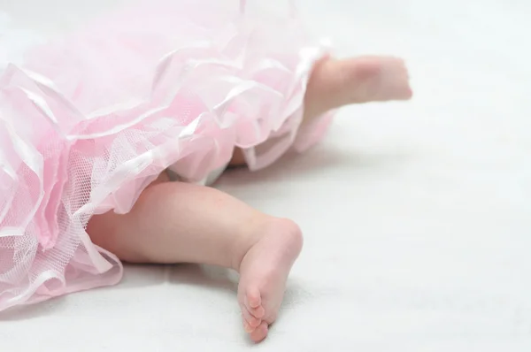 Foots of newborn baby in pink dress Royalty Free Stock Photos