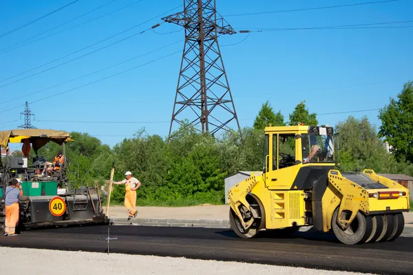 Werknemers met glooiende machines maken asfalt — Stockfoto