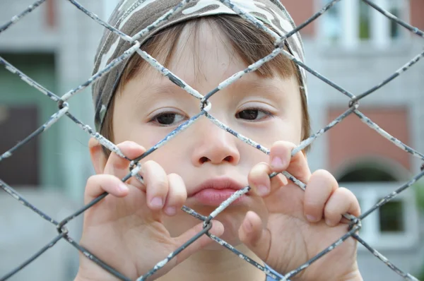 Boy looking sadly behind bars — Stock Photo, Image