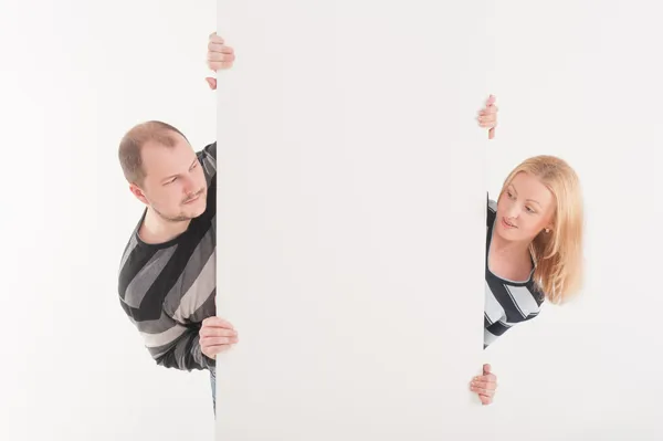 Homem e mulher espreitando atrás de placa em branco no fundo branco — Fotografia de Stock