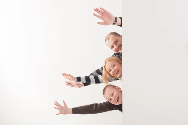 Happy smiling family peeping behind blank board on white backgro — Stock Photo, Image