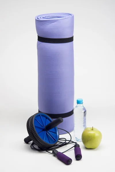 Mat with skipping rope, water bottle, fitness roller and apple — Stock Photo, Image