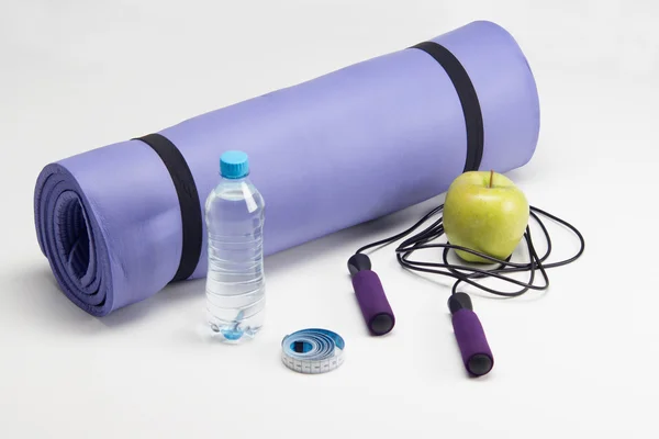 Yoga mat with skipping rope, apple, measuring tape and of water — Stock Photo, Image