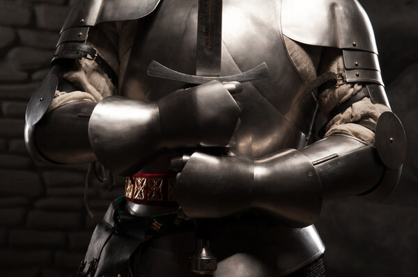 Closeup portrait of medieval knight in armor holding a sword in dark stone wall background