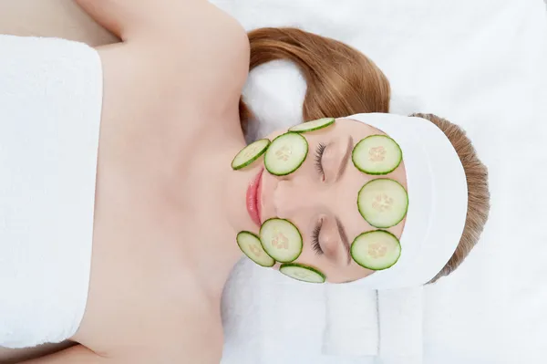 Beautiful young woman receiving facial mask of cucumber in beaut — Stock Photo, Image