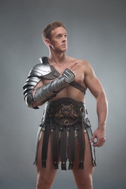 Gladiator in armour posing over grey background clipart