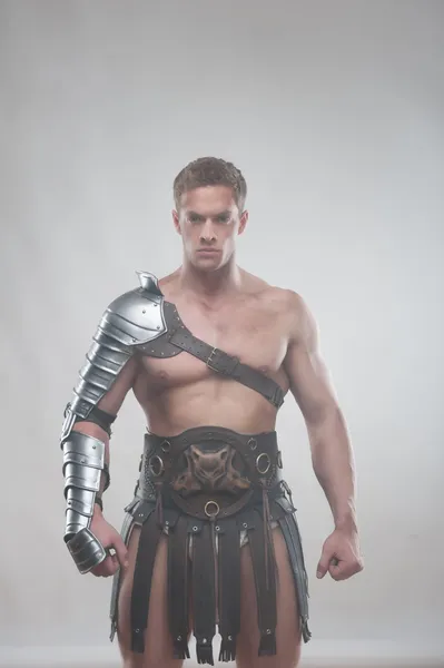 Gladiador em armadura posando sobre fundo cinza — Fotografia de Stock