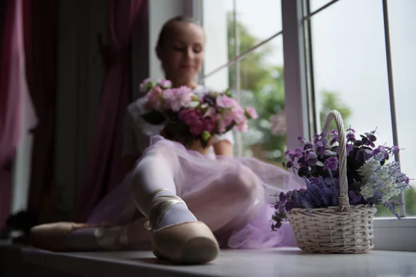 Ballet dancer sitting on windowsill holding flowers — Stock Photo, Image
