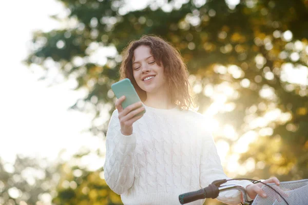 Молодая девушка в парке со смартфоном в руках — стоковое фото