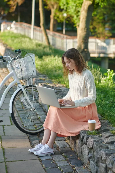 Une jeune fille avec un ordinateur portable assis sur le banc dans le parc — Photo