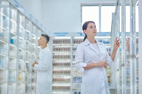 Mujer mirando de cerca los estantes de farmacia y empleado —  Fotos de Stock