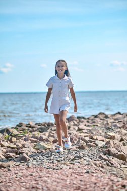 Plajda yürüyen beyaz elbiseli bir kız.