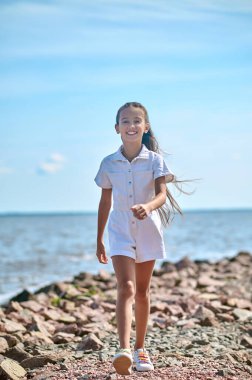 Plajda yürüyen beyaz elbiseli bir kız.